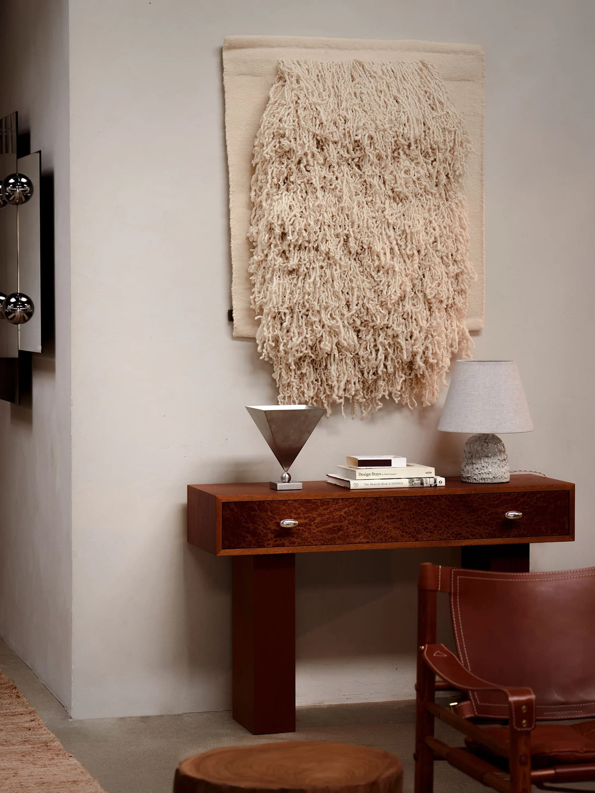 Wooden console with a woven wall hanging, a stone lamp and a leather safari chair