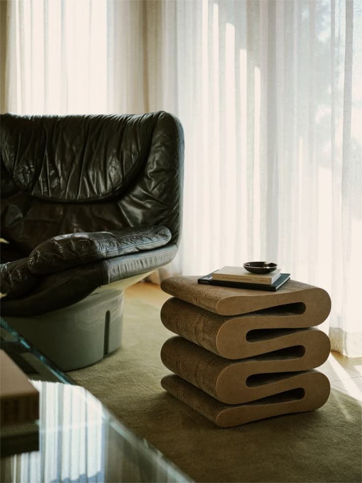 Black leather armchair and a corrugated cardboard side table by a sheer curtain