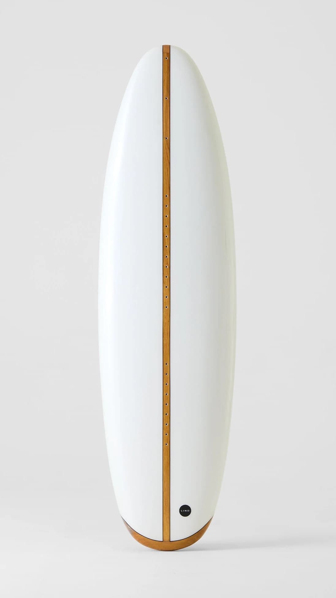 Lind electric surfboard standing upright, white with an oak stringer and the round Lind badge