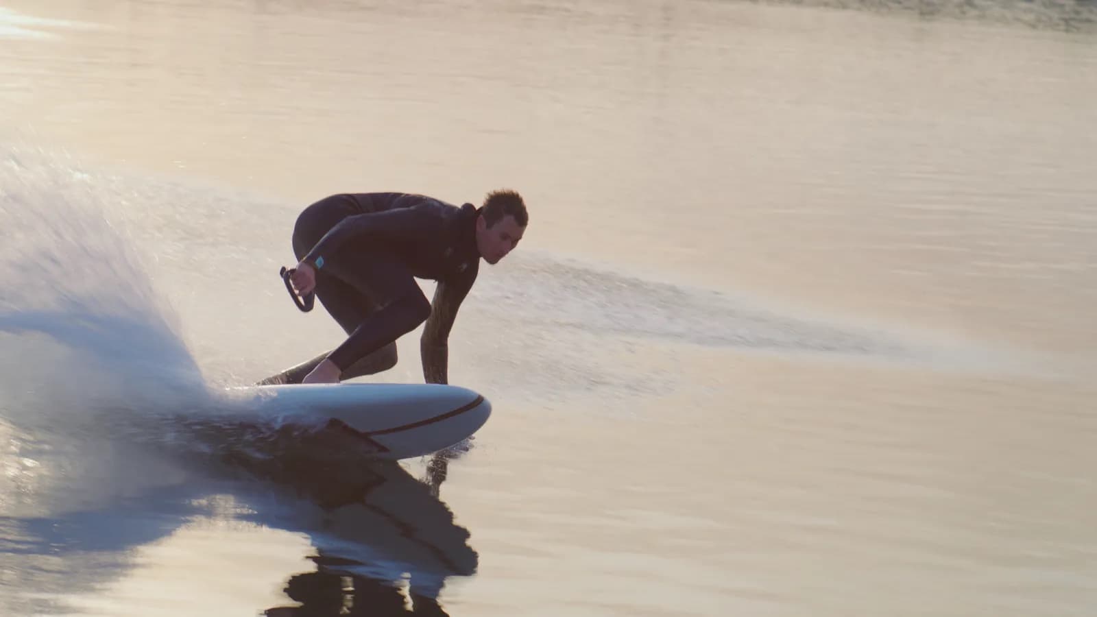 Rider carving on a Lind electric surfboard across calm water at sunset